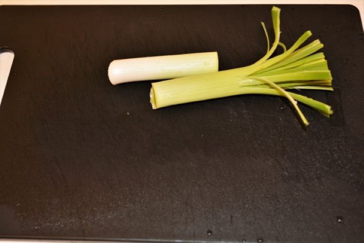 Fresh green leek sliced in half lengthwise on a cutting board.