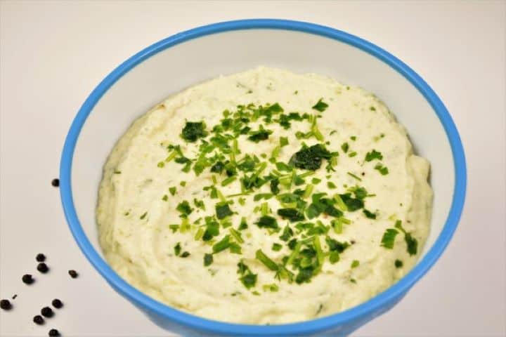Velvety creamy cauliflower spread in a blue serving bowl garnished with fresh chopped parsley.