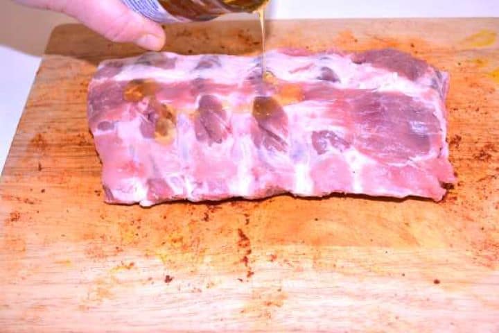 Brushing pure floral honey over raw pork ribs on a chopping board to help the spice rub stick.