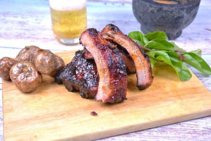 Juicy grilled honey glazed pork ribs served with crisp potato wedges and dipping sauce on a wooden platter.