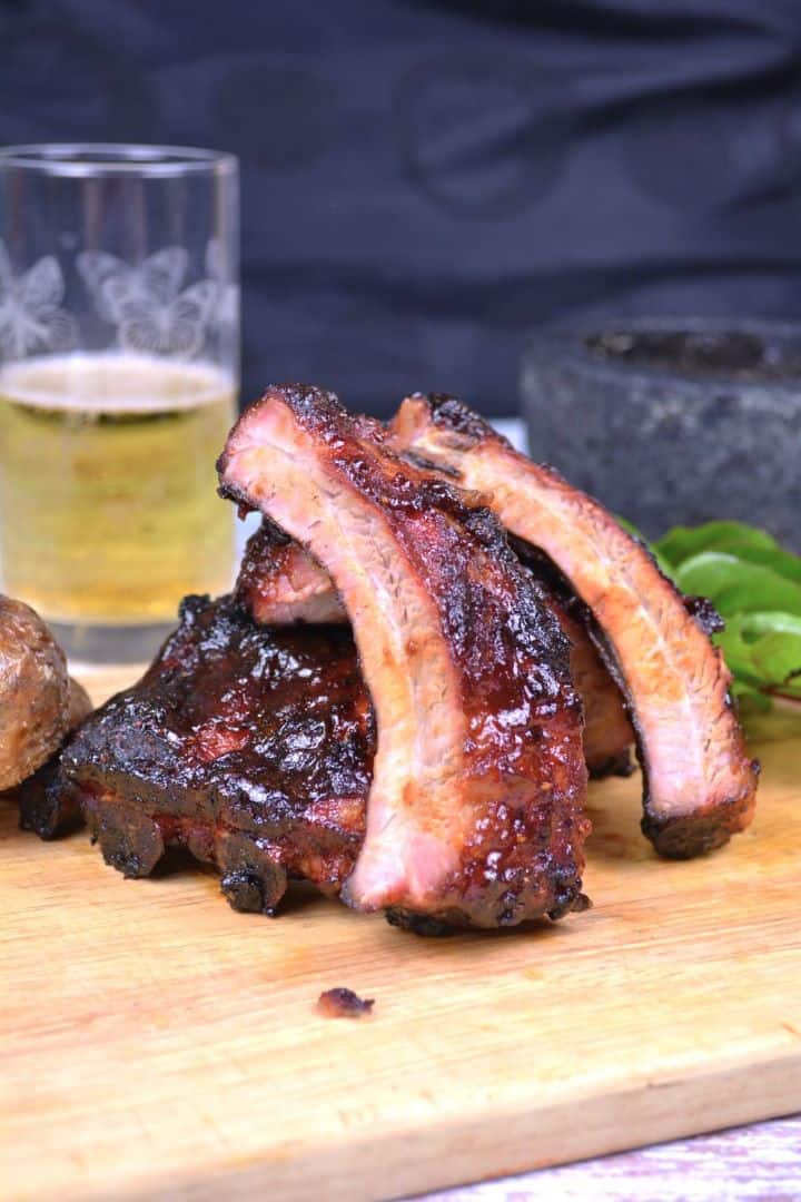 Sticky honey glazed pork ribs sliced on a rustic wooden cutting board with a cold beer and roasted potatoes.