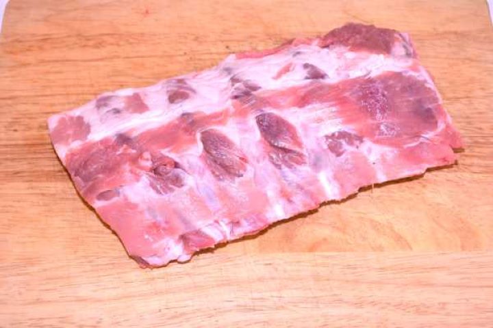 Fresh rack of raw pork ribs on a wooden board prepared for membrane removal and seasoning.