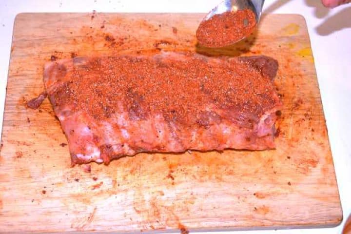 Massaging sweet paprika, brown sugar, and sea salt dry rub evenly across the rack of pork ribs.