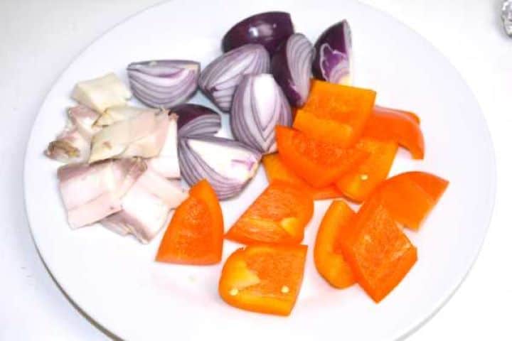 Chopped bell peppers, diced onions, and smoked pork fat cubes arranged on a plate.