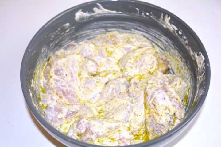 Cubed chicken thighs coated in a spiced Greek yogurt marinade inside a mixing bowl.
