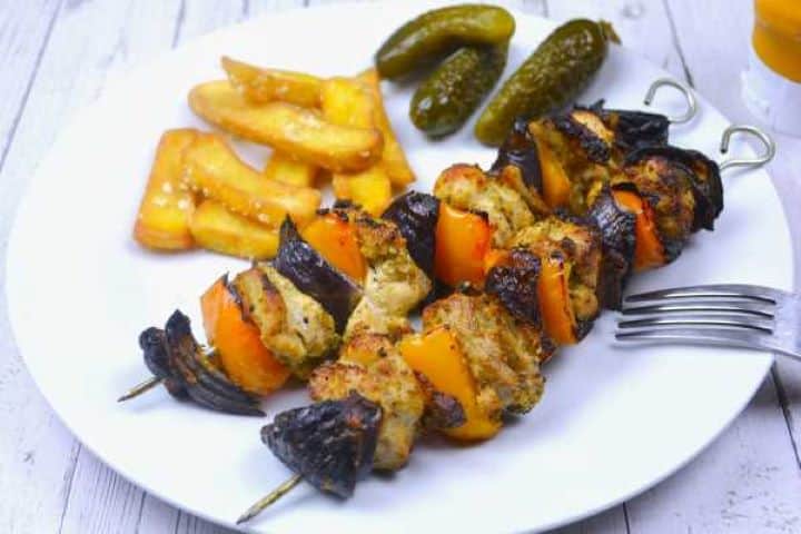 Golden oven baked chicken skewers resting with fries and pickles on a plate.