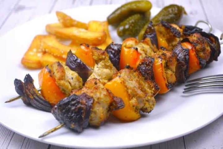 Oven cooked chicken kebabs served on plate with fries.