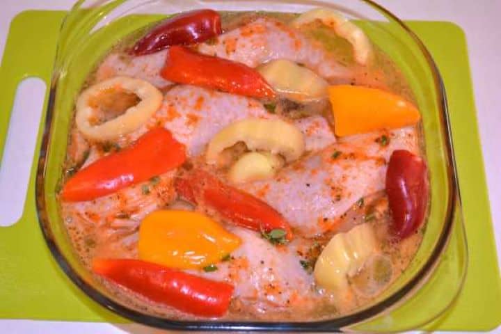 Ready to Bake Pouring beer into a glass casserole dish around seasoned chicken legs and sliced bell peppers.