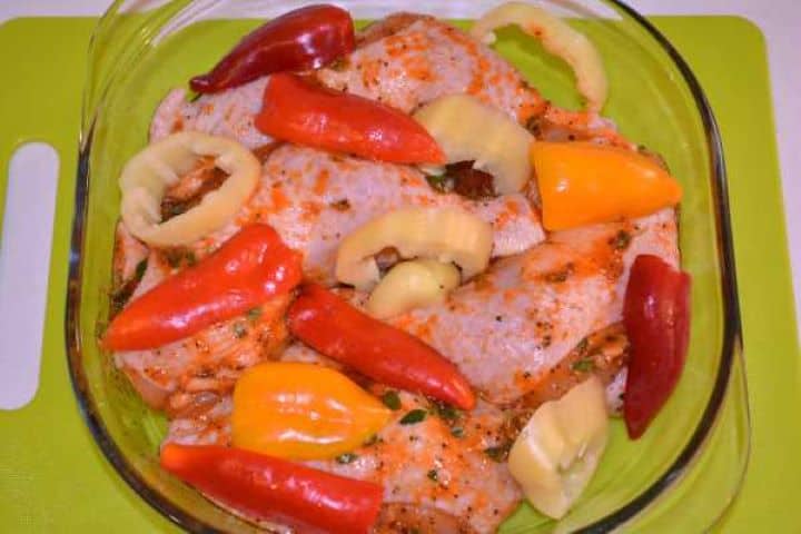 Legs and Peppers Sliced red, yellow, and orange bell peppers scattered over seasoned chicken legs in a glass baking dish.