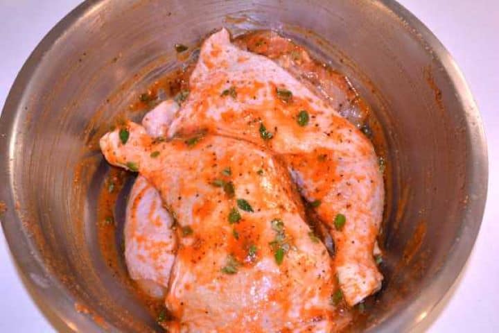 Seasoned Chicken legs thoroughly coated in red sweet paprika paste, honey, and seasoning blend in a bowl.