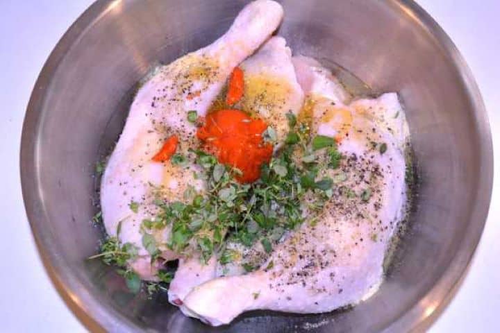 Raw chicken legs in a glass bowl seasoned with sweet paprika paste, honey, thyme, and spices.