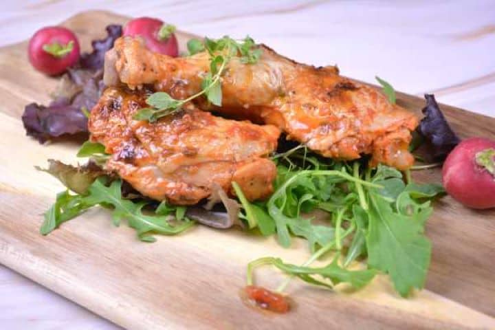 Serving Tender roasted chicken legs plated with sweet pepper gravy, fresh arugula, and radishes on a rustic board.