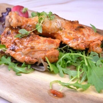 Juicy roasted chicken legs served on a wooden board with fresh wild rocket and sliced radishes.