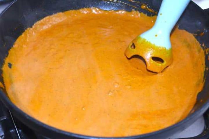 Blending tomato butter chicken sauce with an immersion blender until silky smooth.