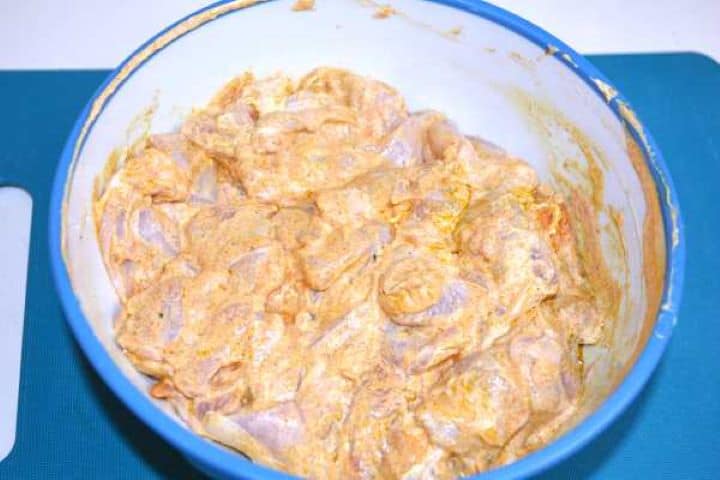 Yogurt-marinated chicken thighs resting in a glass bowl before pan-searing.