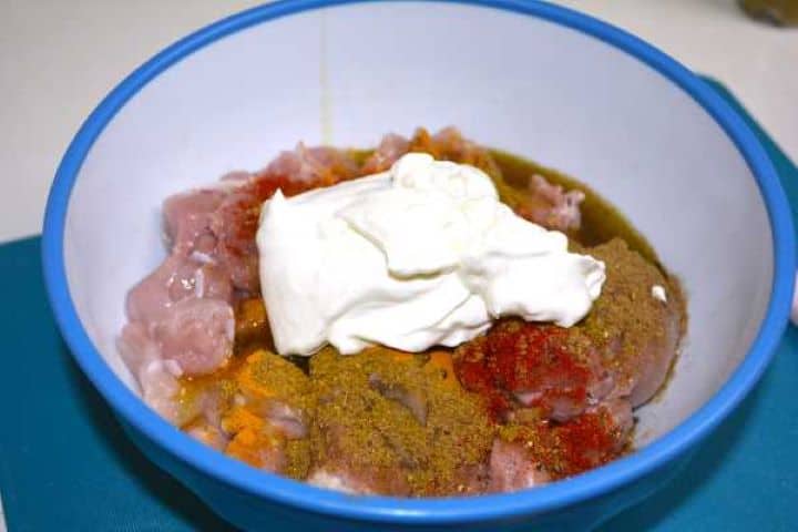 Diced raw chicken thighs topped with Greek yogurt, turmeric, cumin, and garam masala.