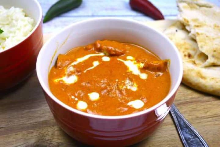 Creamy butter chicken in a bowl served with fresh naan bread and fluffy basmati rice.