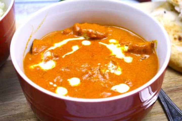 Scooping creamy butter chicken sauce with warm garlic naan bread.
