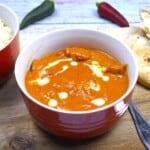 Creamy butter chicken in a red bowl served with fresh naan bread and fluffy basmati rice.