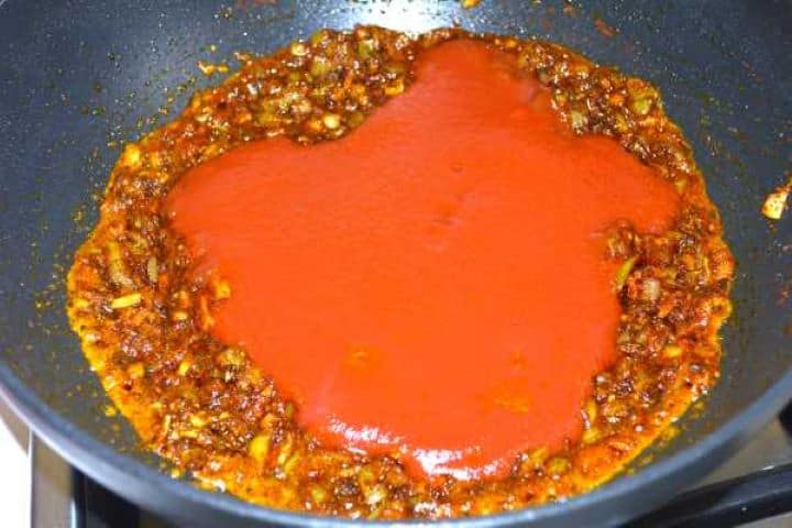 Adding tomato passata to sautéed onions and toasted Indian curry spices.