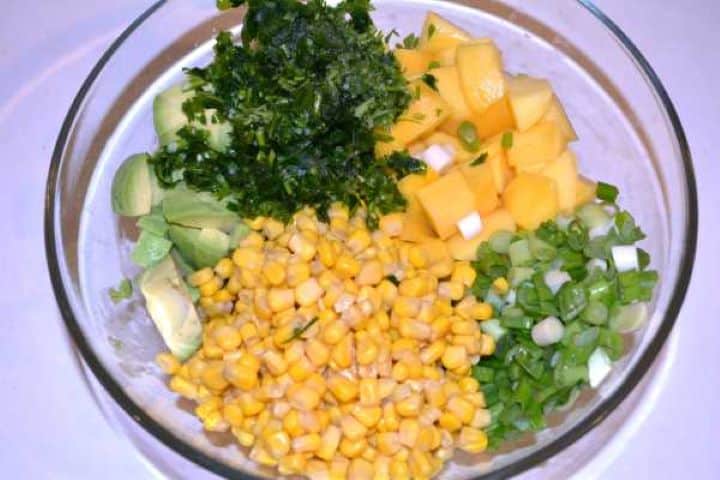 All Ingredients in the Bowl Diced avocado, sweet mango, corn, spring onions, and parsley combined in a glass mixing bowl.