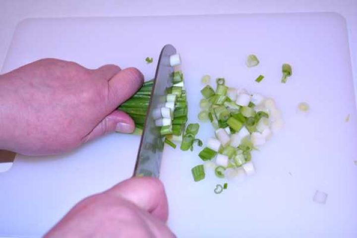 Chopping fresh spring onions on a white cutting board.
