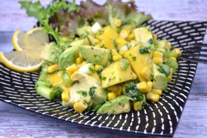 Served Creamy avocado mango corn salad served on a dark decorative plate with fresh citrus.