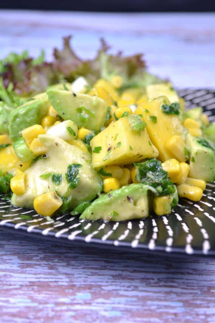 Serving Fresh easy avocado and mango salad served on a white plate with lettuce leaves and lemon slices.
