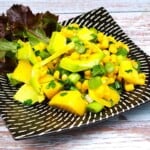 Fresh easy avocado and mango salad served on a white plate with lettuce leaves and lemon slices.