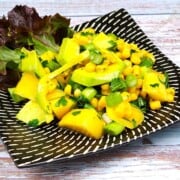 Fresh easy avocado and mango salad served on a white plate with lettuce leaves and lemon slices.