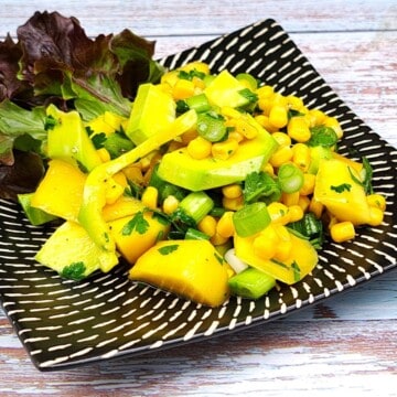 Fresh easy avocado and mango salad served on a white plate with lettuce leaves and lemon slices.