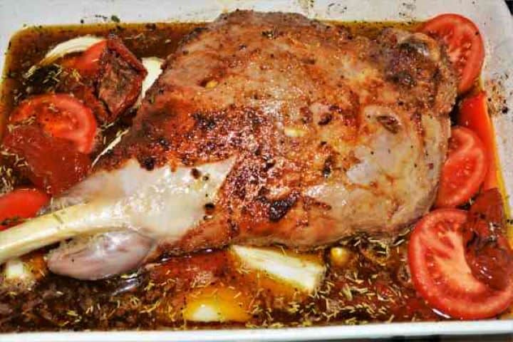 Slow Roasted Leg of Lamb Recipe-Pre-Roasted Lamb Leg With Vegetables Ready to Bake Pre-roasted lamb leg in a tray surrounded by vegetables, bay leaves, and beer-based braising liquid.