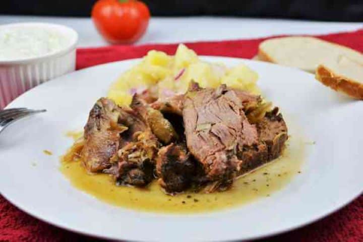 Slow Roasted Leg of Lamb Recipe-Served on Plate With Potato Salad and Tzatziki Close-up of succulent slow-roasted lamb meat pulling away from the bone with a fork.