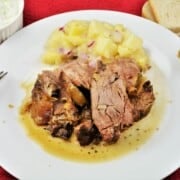Slow-roasted Greek leg of lamb served with potato salad and fresh tzatziki on a plate.