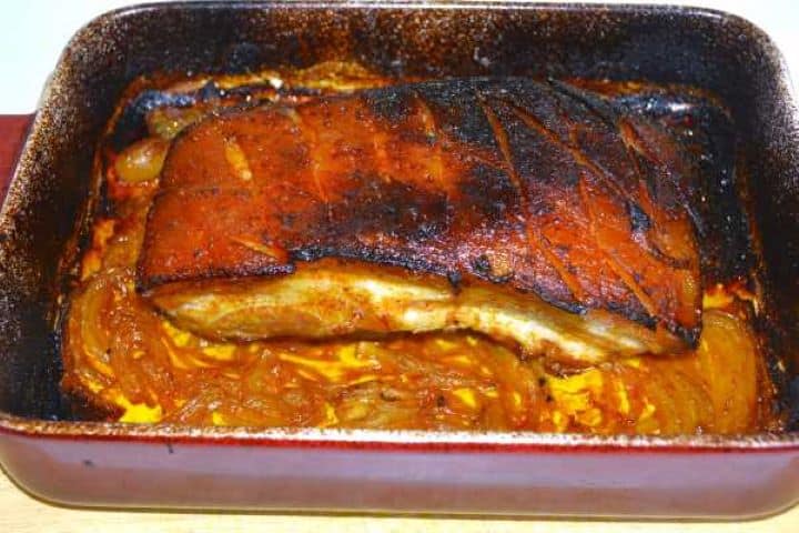 Golden sticky honey glazed pork belly fresh out of the oven in a ceramic baking dish.