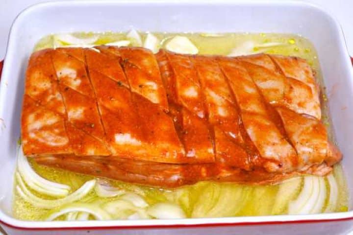 Glazed pork belly resting over onions with lager beer poured into the ceramic baking dish.