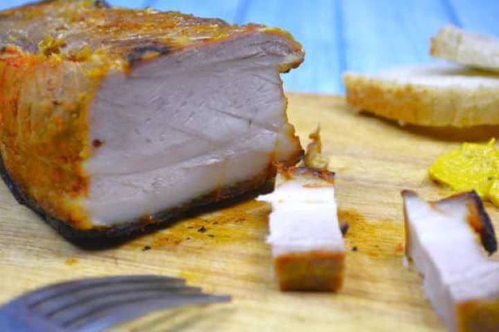 Tender honey glazed pork belly slices presented on a wooden board with crusty bread.