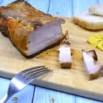 Sliced sticky honey glazed pork belly served on a wooden chopping board with mustard and bread.