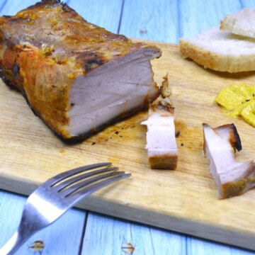 Sliced sticky honey glazed pork belly served on a wooden chopping board with mustard and bread.