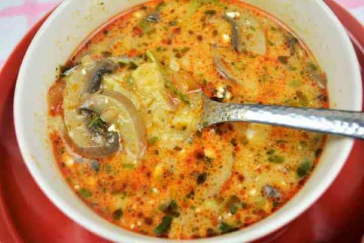Best Mushroom Soup Recipe-Served in Bowl Ladle of hot Hungarian mushroom soup with chunky mushrooms and tender egg dumplings in a red bowl.