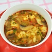 Cozy red bowl of authentic Hungarian mushroom soup with homemade nokedli dumplings and fresh parsley.