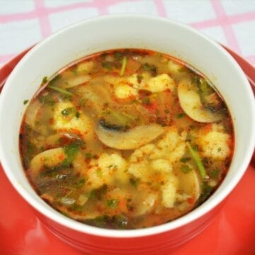 Cozy red bowl of authentic Hungarian mushroom soup with homemade nokedli dumplings and fresh parsley.
