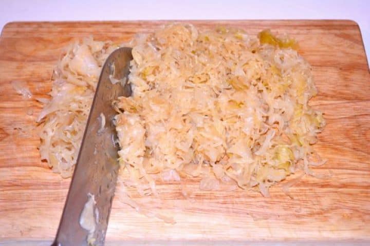 Layered Sauerkraut Casserole-Cut the Sauerkraut on the Chopping Board Chopping shredded sauerkraut strands into smaller pieces on a wooden board.