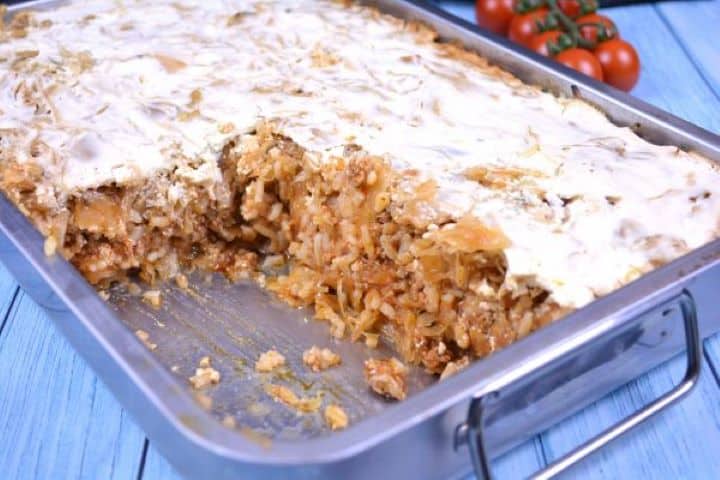 Layered Sauerkraut Casserole-Served in Baking Dish Freshly baked layered sauerkraut casserole with a bubbling golden-brown sour cream crust in a steel baking dish.