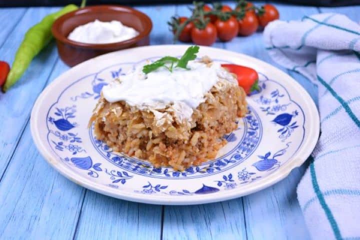 Layered Sauerkraut Casserole-Served on Plate With Sour Cream on the Top Traditional Transylvanian Kolozsvári rakott káposzta served with sour cream on a dinner plate.