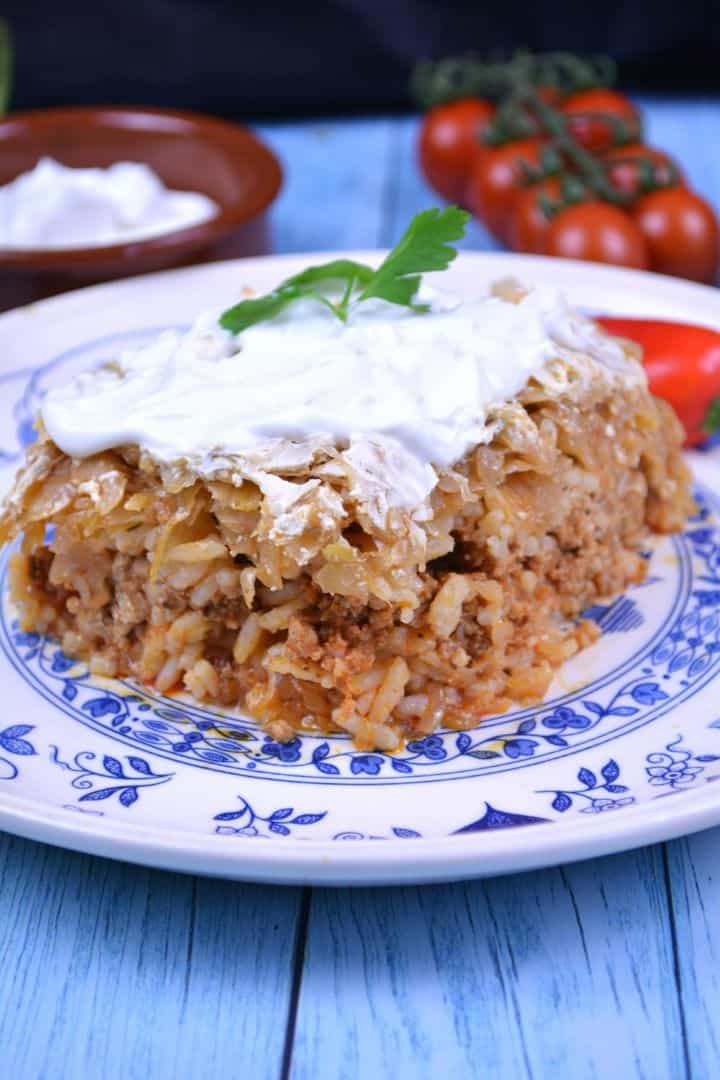 Layered Sauerkraut Casserole-Served on Plate With Sour Cream on the Top Square slice of layered sauerkraut casserole on a white plate topped with a dollop of sour cream.