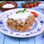 Square slice of layered sauerkraut casserole on a white plate topped with a dollop of sour cream.