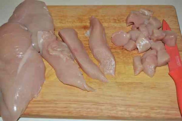 Chicken Breast With Pineapple-Cutting Chicken Breast in Cubes Raw chicken breasts being diced into 1-inch uniform cubes on a cutting board.