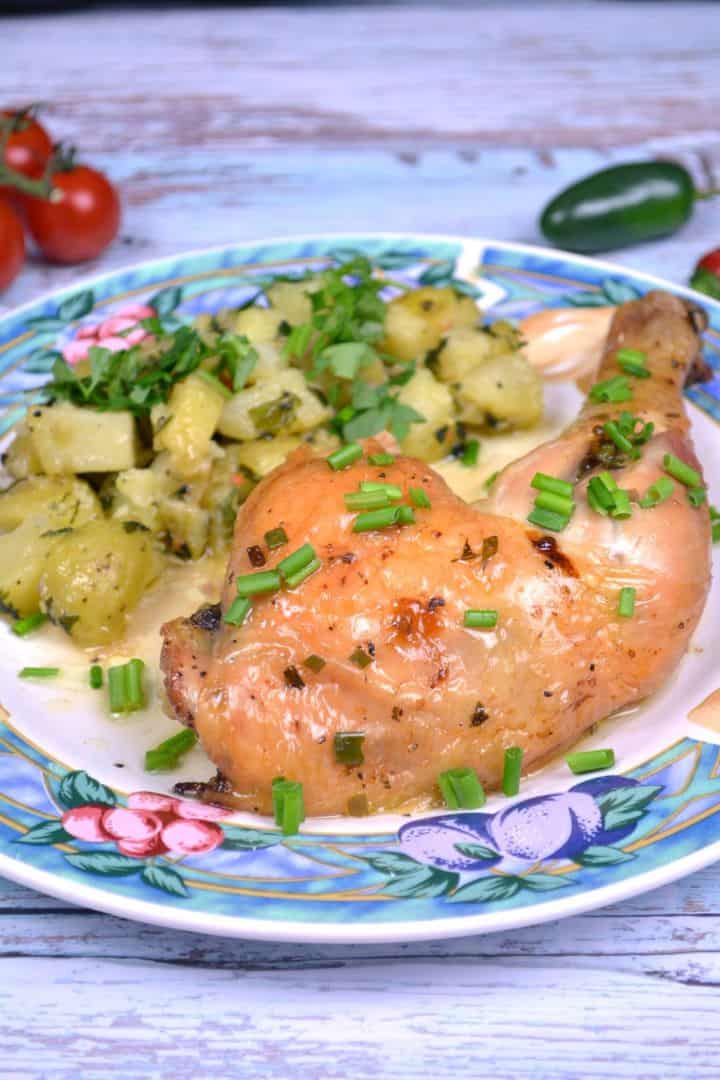 Plated spatchcock garlic butter chicken leg served with potato salad and fresh chives.