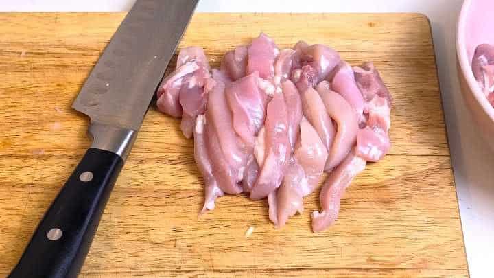 Boneless skinless chicken thighs cut into bite-sized strips on a chopping board.
